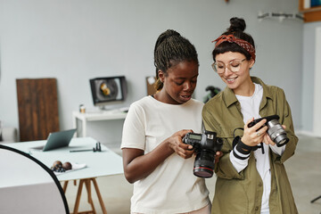 Waist up portrait of two female photographers holding cameras while working in photo studio, copy...