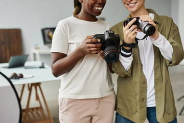 Cropped shot of two smiling female photographers holding cameras while working in photo studio,...