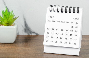 April 2022 desk calendar with plant pot on wooden table.