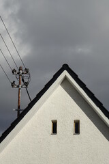 Fototapeta na wymiar Power pole with grounding on white gable, dramatic stormy sky, concept: energy, electricity, power, supply, dependence, threat (vertical), Dahlbruch, NRW, Germany
