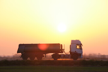 Fototapeta premium Semi-truck with tipping cargo trailer transporting sand from quarry driving on highway hauling goods in evening. Delivery transportation and logistics concept