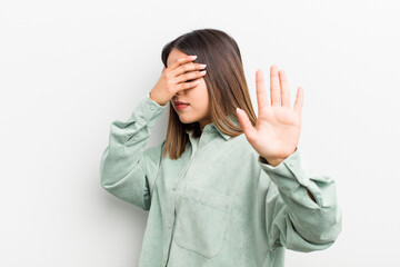 pretty hispanic woman covering face with hand and putting other hand up front to stop camera,...