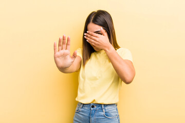pretty hispanic woman covering face with hand and putting other hand up front to stop camera,...