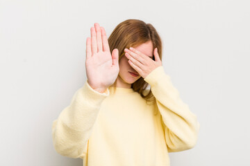 red head pretty woman covering face with hand and putting other hand up front to stop camera,...
