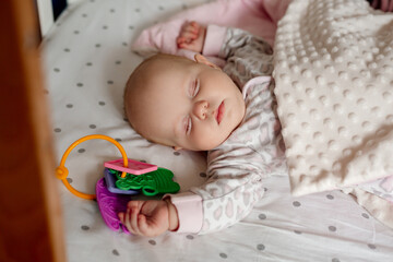 newborn baby covered with a blanket sleeps in his crib with his favorite toy. happy carefree infancy