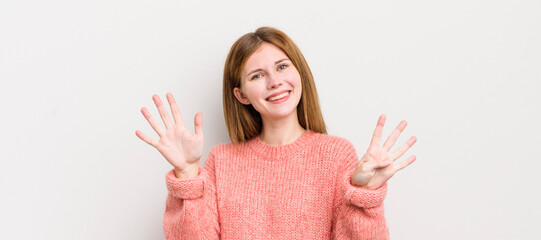 red head pretty woman smiling and looking friendly, showing number nine or ninth with hand forward,...