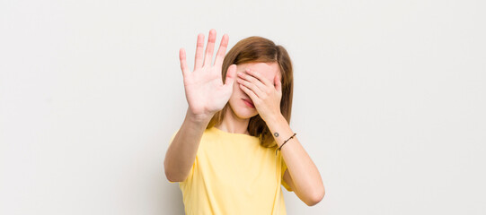 red head pretty woman covering face with hand and putting other hand up front to stop camera,...