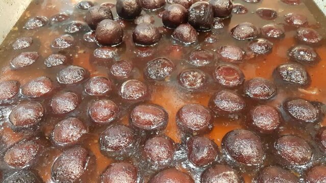 Indian Traditional Juicy Gulab Jamun in Large Steel Pan available for sale in the market. The Indian sweet Gulab jamun. Gulab jamuns indian desserts. Pan Full of Syrup Laden Gulab Jamuns. 
