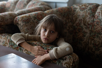 Sad little girl hiding behind sofa at home. Domestic violence concept