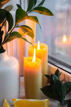Yellow bee wax candles near window. Firelight. White vase