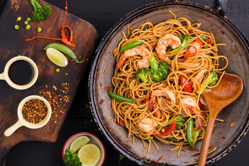 Stir-fried spaghetti or stir-fry noodles with vegetables and shrimp in a black frying pan. dark background, top view
