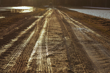 tire tracks on dirty muddy wet sand and gravel road in sunset light