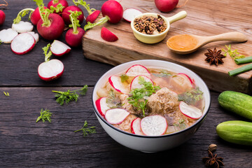 Hot soup with radish, cucumber, and parsley on a wooden table