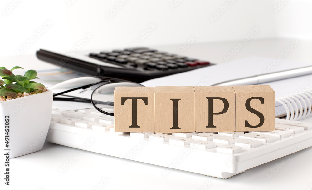 Poster tips written on a wooden cube on keyboard with office tools