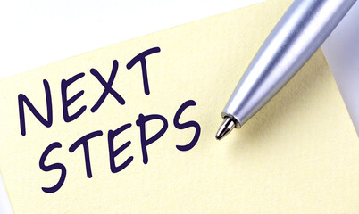 Sticky Note Message NEXT STEPS with pen on white background