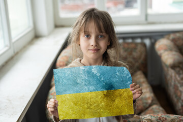Sad little girl covered with Ukraine flag. Concept of standing with Ukrainian nation in war with Russia