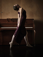 Sensual female dancer bending back standing near piano