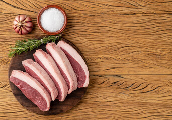Sliced raw picanha or rump meat over wooden board with seasonings and copy space
