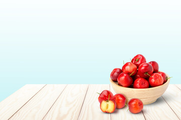 Acerola cherry in wooden bowl on white wooden table with blue background. Copy space for text.