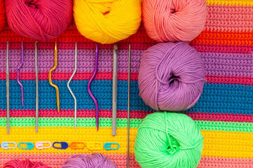 All for hand knitting. Knitted multi-colored handmade fabric with balls of multi-colored threads, pins and various knitting needles on it.