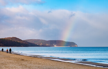 Panoramic winter view of Baltic sea with people walking along beach offshore Gdynia Orlowo of Tricity with rainbow in Pomerania region of Poland