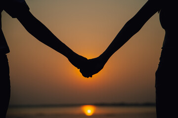 Young couple in love holding hands looking in the sunset