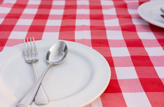 Close up and selective focus of ceramic dish with prepared steel fork and spoon on red checkered pattern dining cloth shows dining preparation in restaurant for serving lunch and dinner meal.