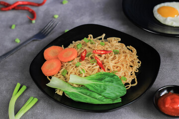 Mie Goreng. Fried noodles served with fried eggs and vegetables on a plate.