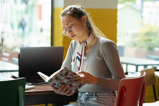 Young girl with glasses reading a book in a cafe