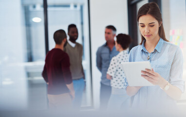 Checking a few emails. Cropped shot of a young businesswoman working in the office with her colleagues in the background.