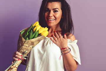 Attractive pleased  Lovable  Beautiful Smiling  Grateful  Woman receives flowers as present, stands with closed eyes, enjoys her favorite   Yellow, isolated on  purple background. Romantic portrait.