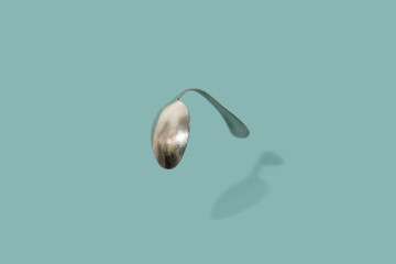 Curved kitchen metal spoon from matrix on green backround.