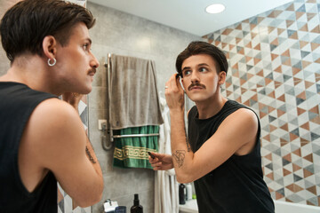 Man with clear healthy skin, using brow gel on his eyebrows and looking in mirror
