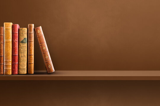 Row of old books on brown shelf. Horizontal background
