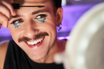 Metrosexual man with mustaches holding make up brush near his face and laughing