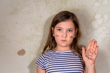 Stop war in Ukraine concept. Little Ukrainian blond girl, with the flag of ukraine in the heart in a ruined old house. Save the children, close the sky of Ukraine, humanitarian aid disaster concept