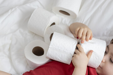 little boy sitting on the bed and playing with toilet paper. kid boy sitting at home and looking...