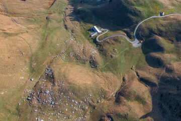 Aerial view of a farm located in a hilly expanse, and a winding road winding through the hills to reach the farm.