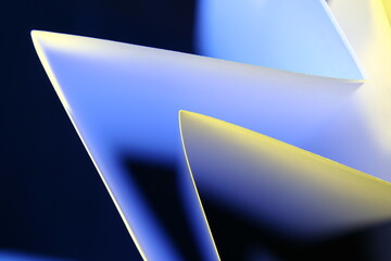 Triàngulos de papel blanco con luz transversal rasante de color azul y amarillo, forma un bello...