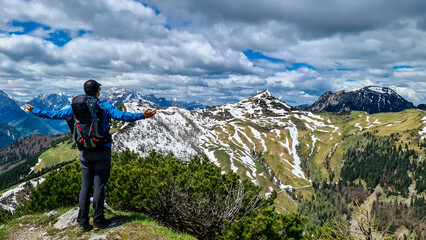 Hiker man with backpack at summit of Hahnkogel (Klek) with scenic view on mountain peaks in Karawanks and Julian Alps, Carinthia, Austria. Border with Slovenia. Triglav National Park. Spreading arms