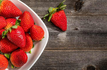 Fresh strawberries i a white bowl on a antique wooden board