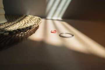 Close up of an elegant engagement diamond ring on wood floor with hat, sunlight and shadow...