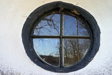 Altes rundes Kirchenfenster mit Spiegelung von Bäumen und Himmel bei Sonne im Winter
