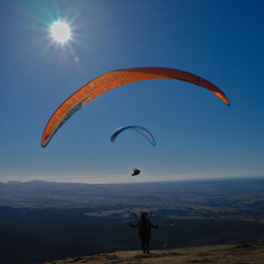 paragliding flight as a couple facing the sun against a background of blue sky in Auvergne