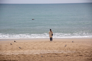 Alone woman is thinking on the beach , pigeon on the sand , looking to sea