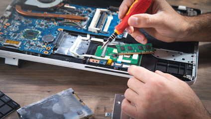 Technician repairing laptop with a screwdriver.