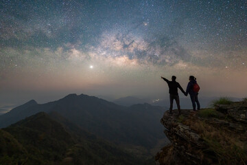 Portrait of an Asian couple, tourists, travel at Doi Tung, Chiang Rai, Thailand with mountain hills, the milky way in galaxy with stars at night. Universe space landscape background. People lifestyle.