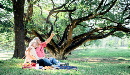 Asian elderly couple, attractive wife and husband, picnic, drinking tea and relaxing on the green lawn in garden, are smile and happy together, to relationship of retirement age and nature concept.