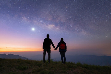 Portrait of an Asian couple, tourists, travel at Doi Tung, Chiang Rai, Thailand with mountain hills, the milky way in galaxy with stars at night. Universe space landscape background. People lifestyle. - obrazy, fototapety, plakaty