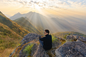 Fototapeta premium Portrait of Asian man, a tourist or backpacker, travel on green mountain hills with fog on holiday vacation. Nature landscape background, Thailand. People lifestyle.